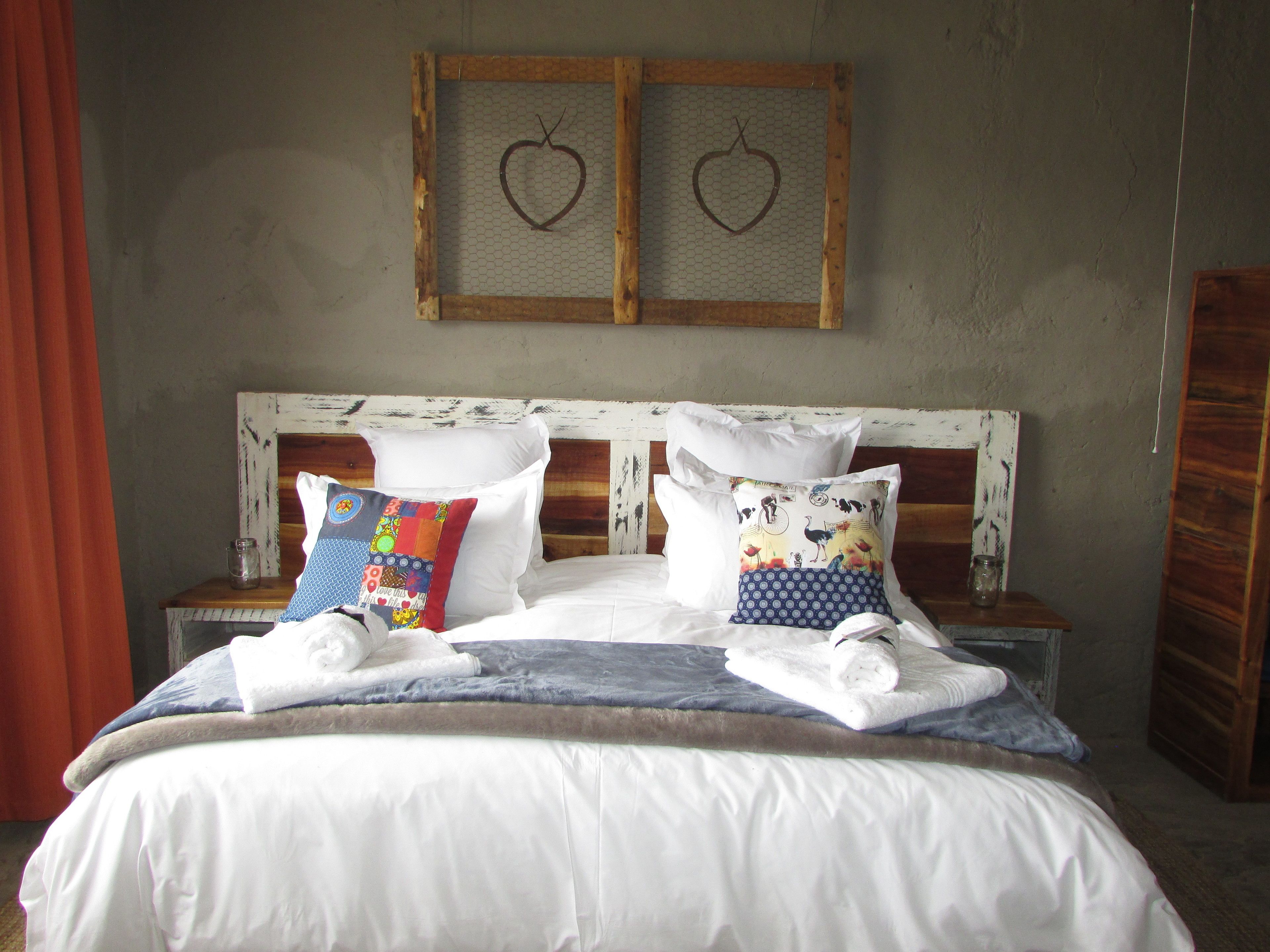 Una cama con sábanas blancas, dos adornos en forma de corazón en la pared y un cabecero de madera.