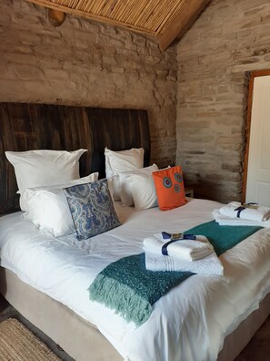A bed with white bedding, a wooden headboard, and several pillows, including a blue patterned one. - Rogge Cloof (Karoo Hoogland)