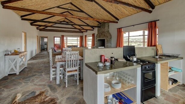A rustic kitchen with a stone floor, wooden beams, a central island with a stove, and a stone fireplace. - Rogge Cloof (Karoo Hoogland)