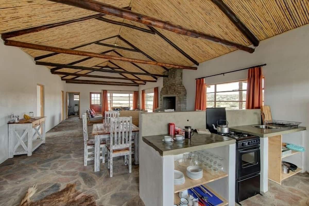 A rustic kitchen with a stone floor, wooden beams, a central island with a stove, and a stone fireplace.