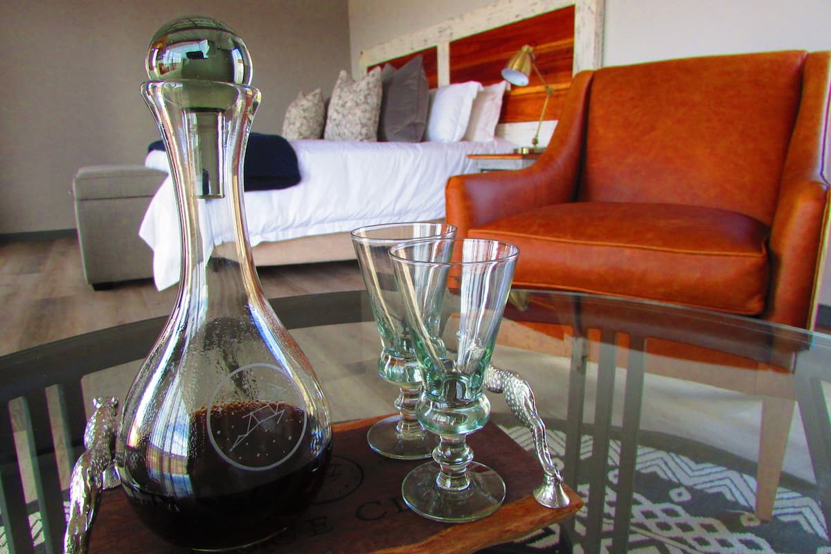 A room with a bed, a glass table with a bottle and glasses, and an orange sofa.