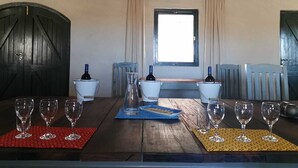 A dining table with wine glasses and bottles, a window with curtains, and a rustic ceiling. - Rogge Cloof (Karoo Hoogland)