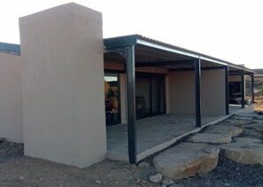 A modern building with a covered patio area, large windows, and a stone pathway leading to the entrance. - Rogge Cloof (Karoo Hoogland)