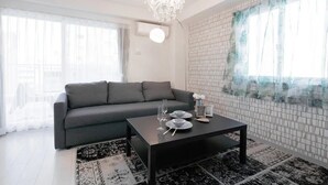 A modern living room with a grey sofa, a black coffee table, and a chandelier. - Hatch NAGAHORI 901 (Osaka)