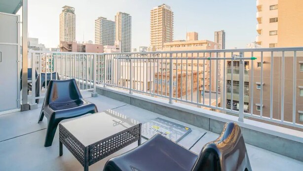 A balcony with a view of tall buildings, a white railing, and a table with chairs. - Hatch NAGAHORI 901 (Osaka)