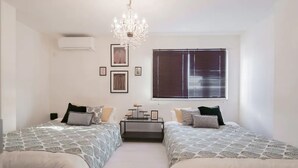 A bedroom with two beds, a chandelier, a window with blinds, and framed pictures on the wall. - Hatch NAGAHORI 901 (Osaka)