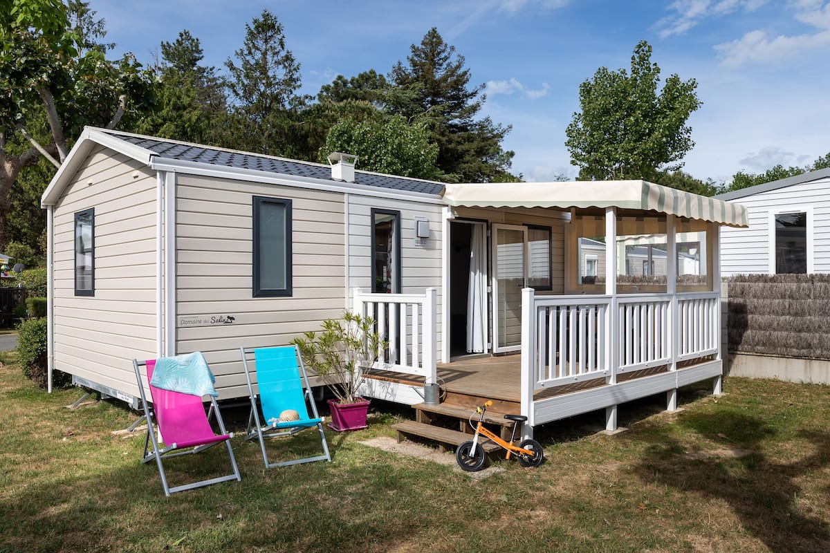 A mobile home with a porch, two lawn chairs, a bicycle, and a potted plant.