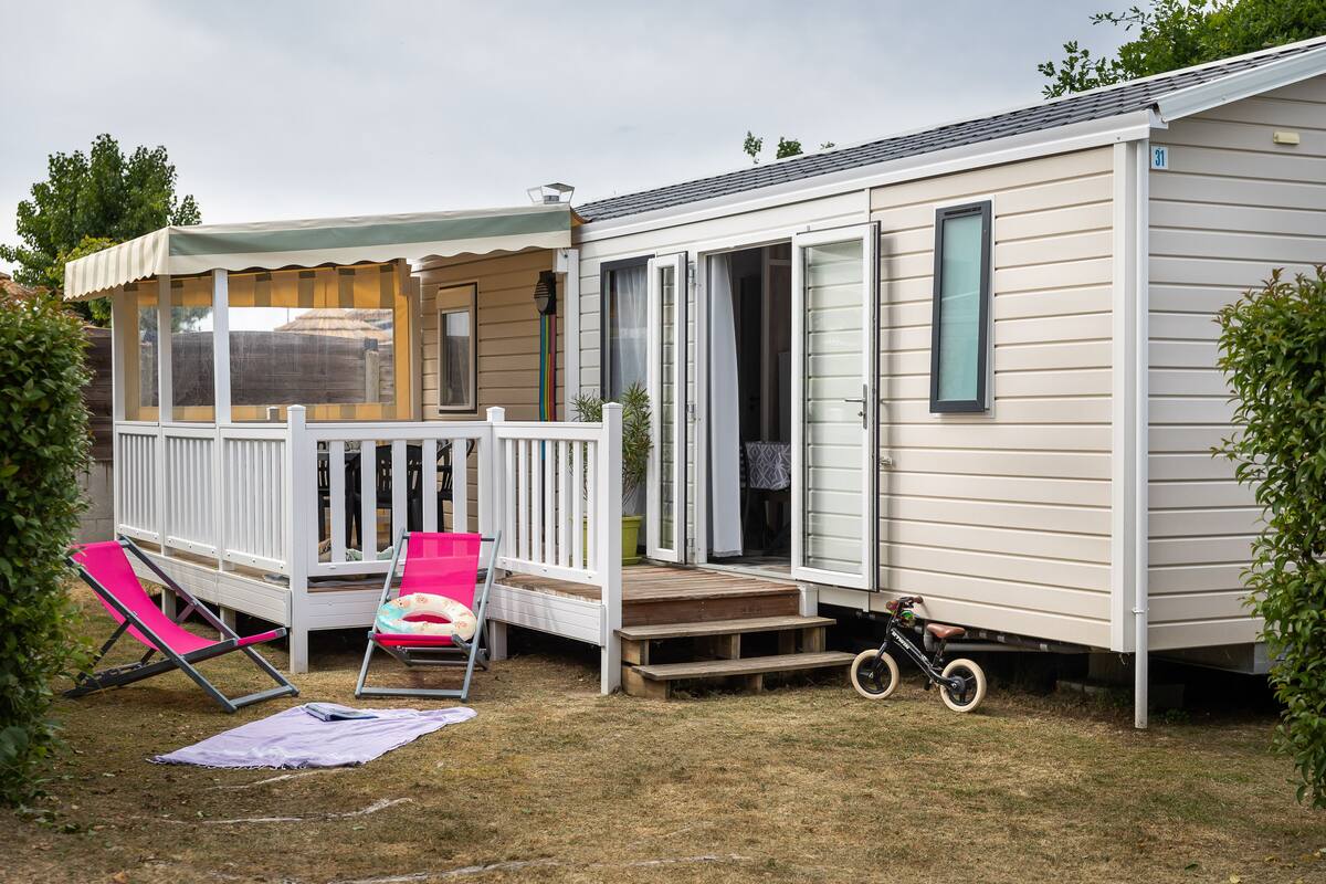 A mobile home with a covered porch, a small deck, and a bicycle parked outside.