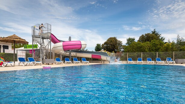 Una piscina con tobogán de agua, sillas de descanso y una torre de salvavidas.
