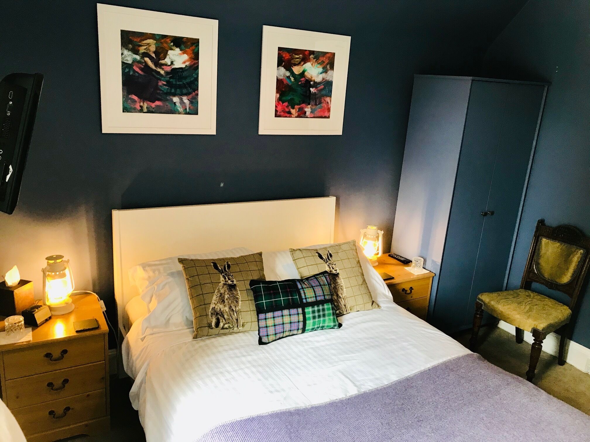A bedroom with a bed, nightstands, a chair, a wardrobe, and two framed pictures on the wall.