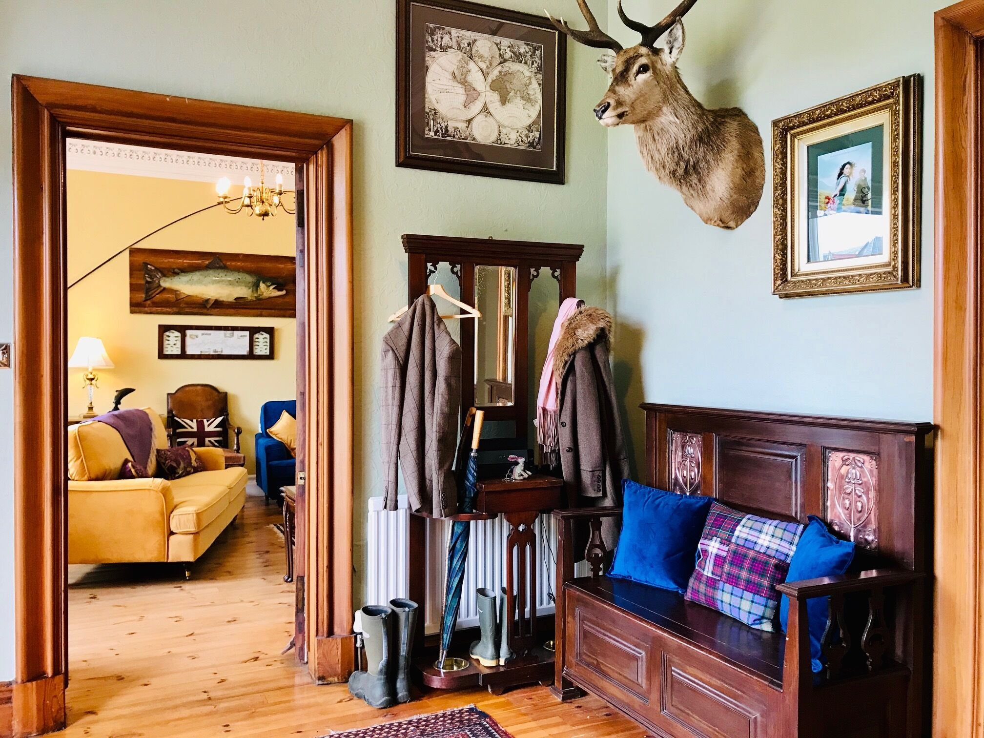 A cozy room with a wooden floor, a blue sofa, a wooden cabinet, and a deer head mounted on the wall.
