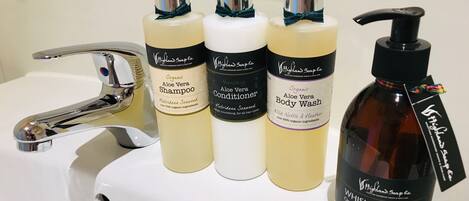 A bathroom sink with four bottles of Highland Soap Co. products: Organic Aloe Vera Shampoo, Nourishing Aloe Vera Conditioner, Organic Aloe Vera Body Wash, and Whiskey & Honey Organic Aloe Vera Hand Wash.