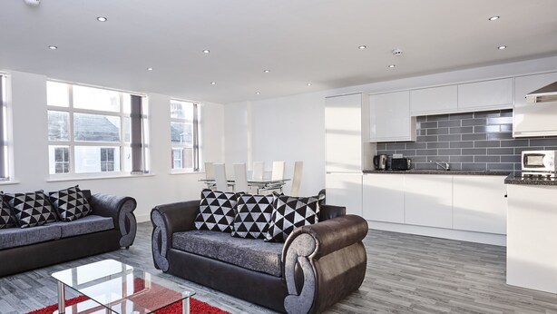 A modern living room with a sofa, a glass coffee table, and a red rug. - Winter Gardens Service Apartments 2 (Blackpool)