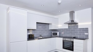 A modern kitchen with white cabinets, a microwave, a toaster, and a stove. - Winter Gardens Service Apartments 2 (Blackpool)