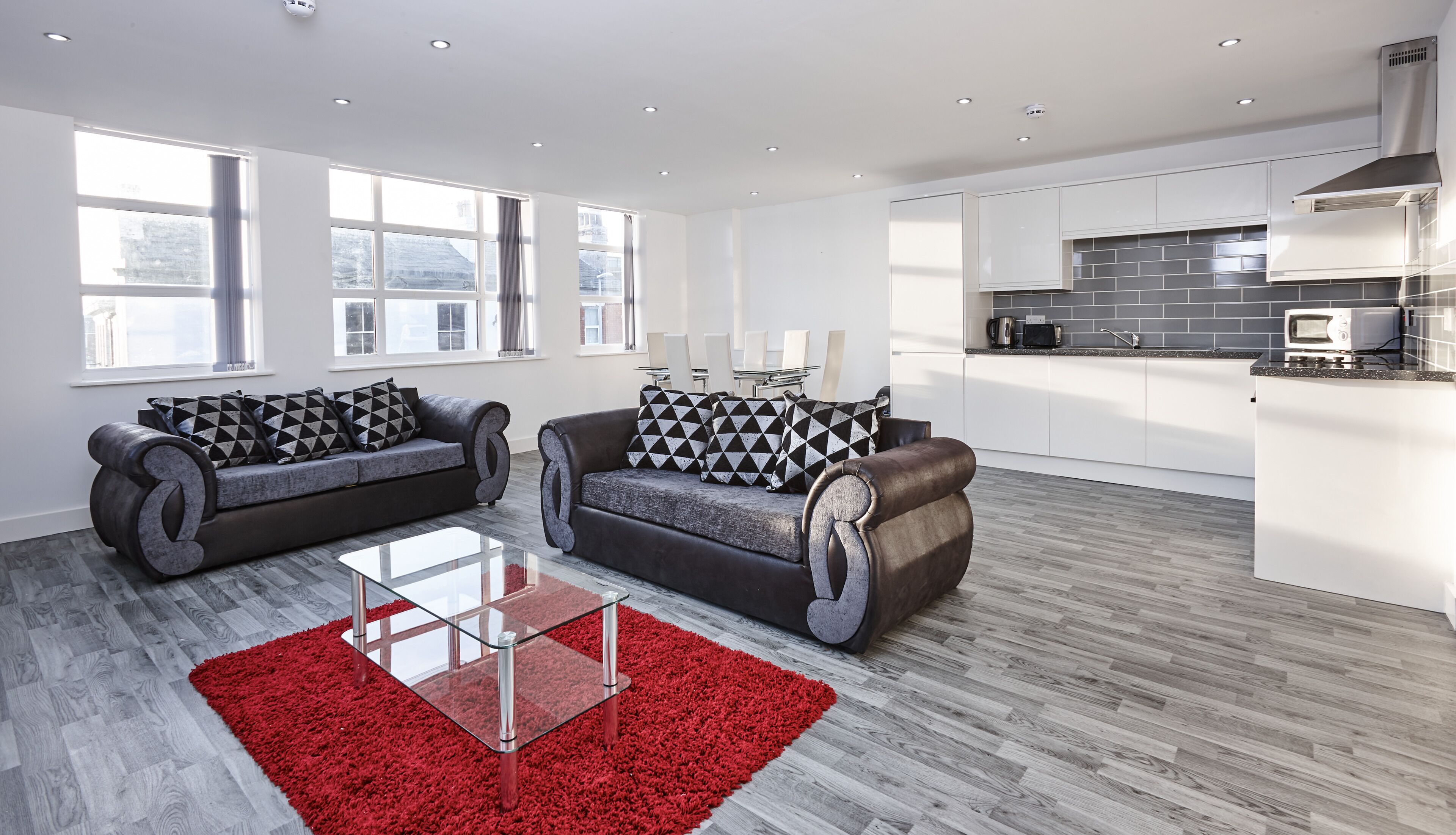 A modern living room with two sofas, a glass coffee table, and a red rug.
