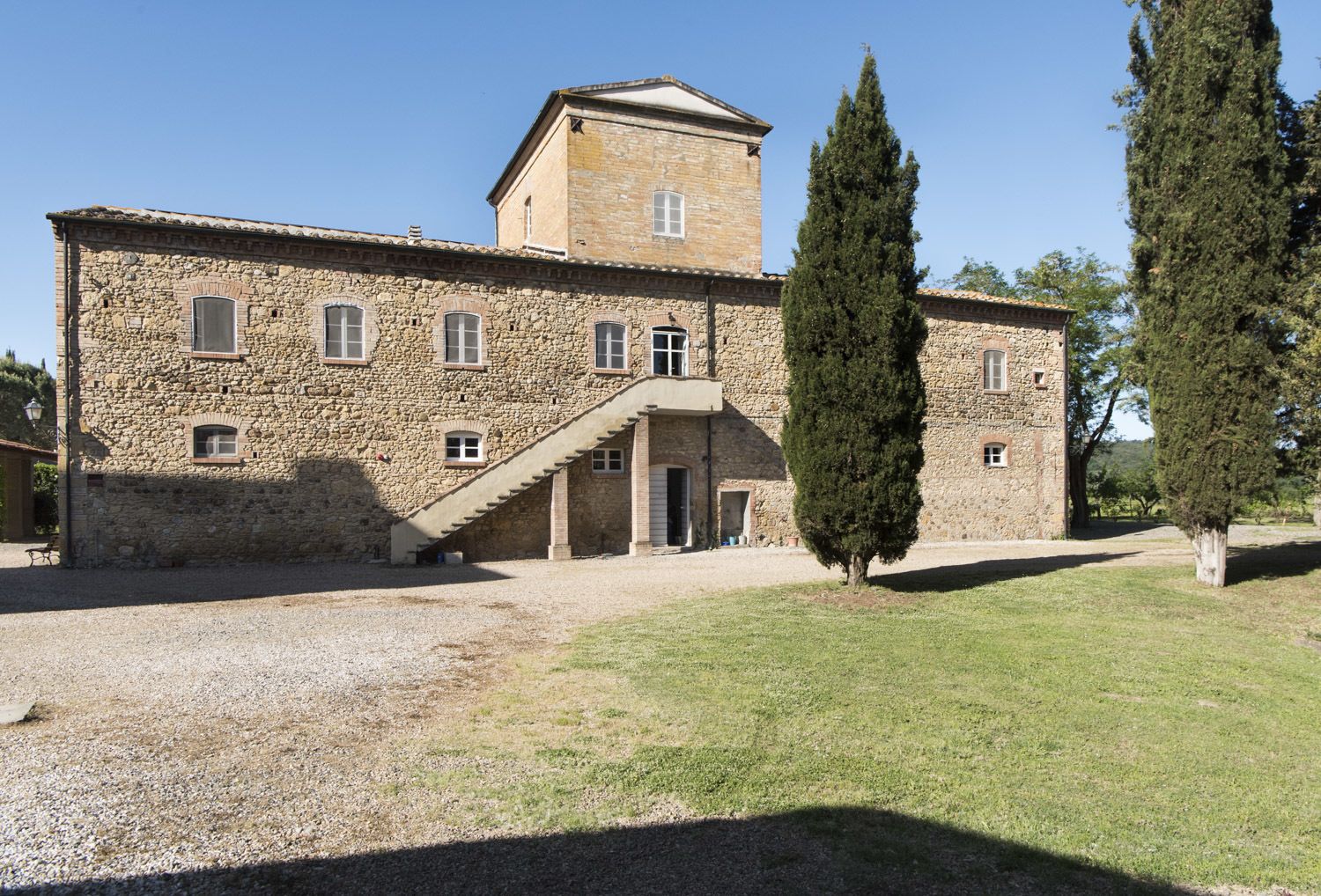 A stone building with a central staircase, a small tower, and a gravel courtyard.