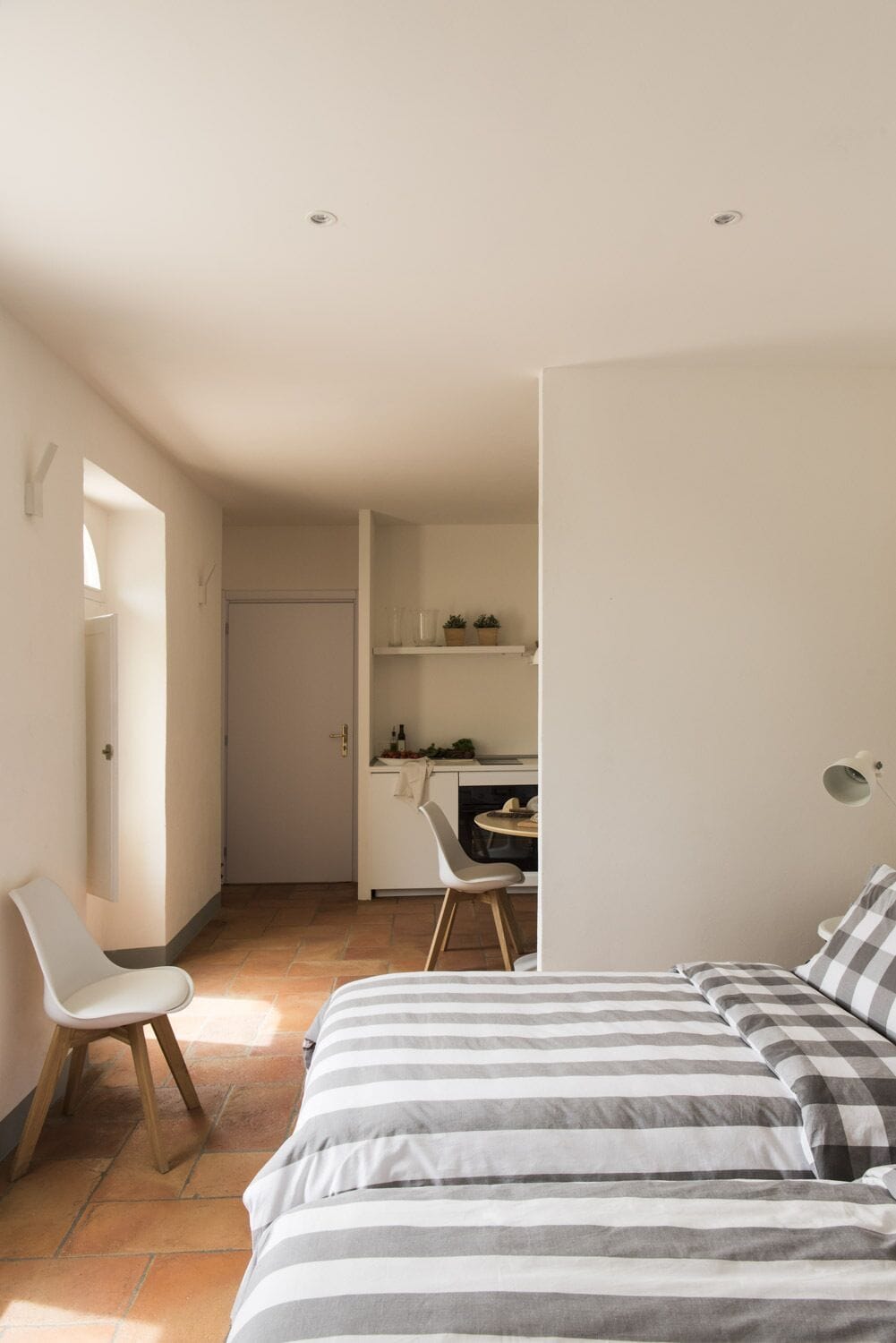 Une chambre à coucher au style minimaliste, avec un lit, une chaise et, au fond, une petite kitchenette.