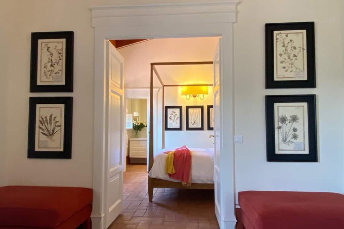 Een slaapkamer met een hemelbed, een rode bank en ingelijste botanische prints aan de wanden.