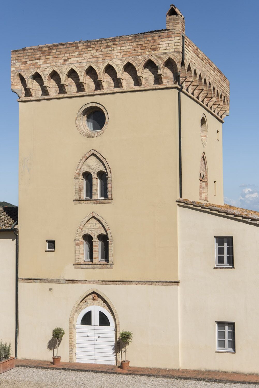 A building with a beige facade, a tower with arched windows, and a small door with a white shutter.