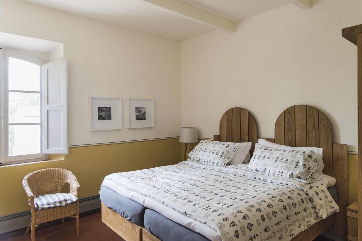 A bedroom with a bed, a chair, a window, and two framed pictures on the wall.