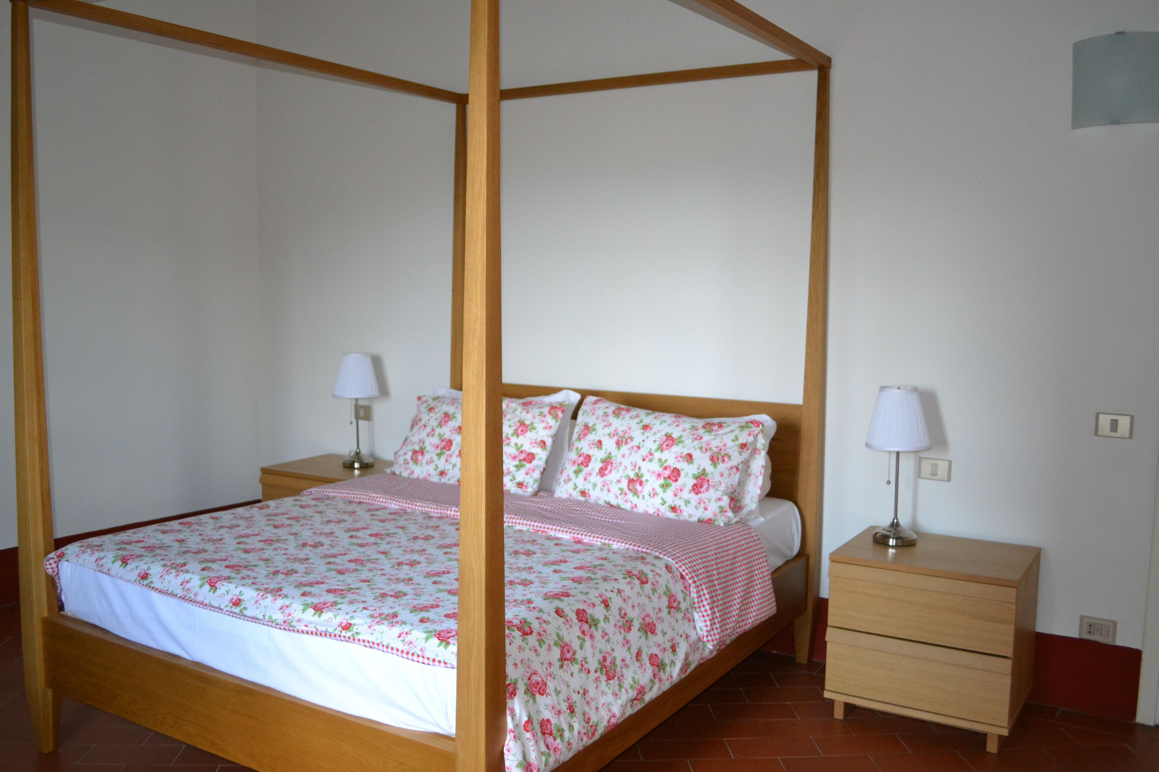 A four-poster bed with floral bedding, two bedside tables with lamps, and a wooden nightstand.