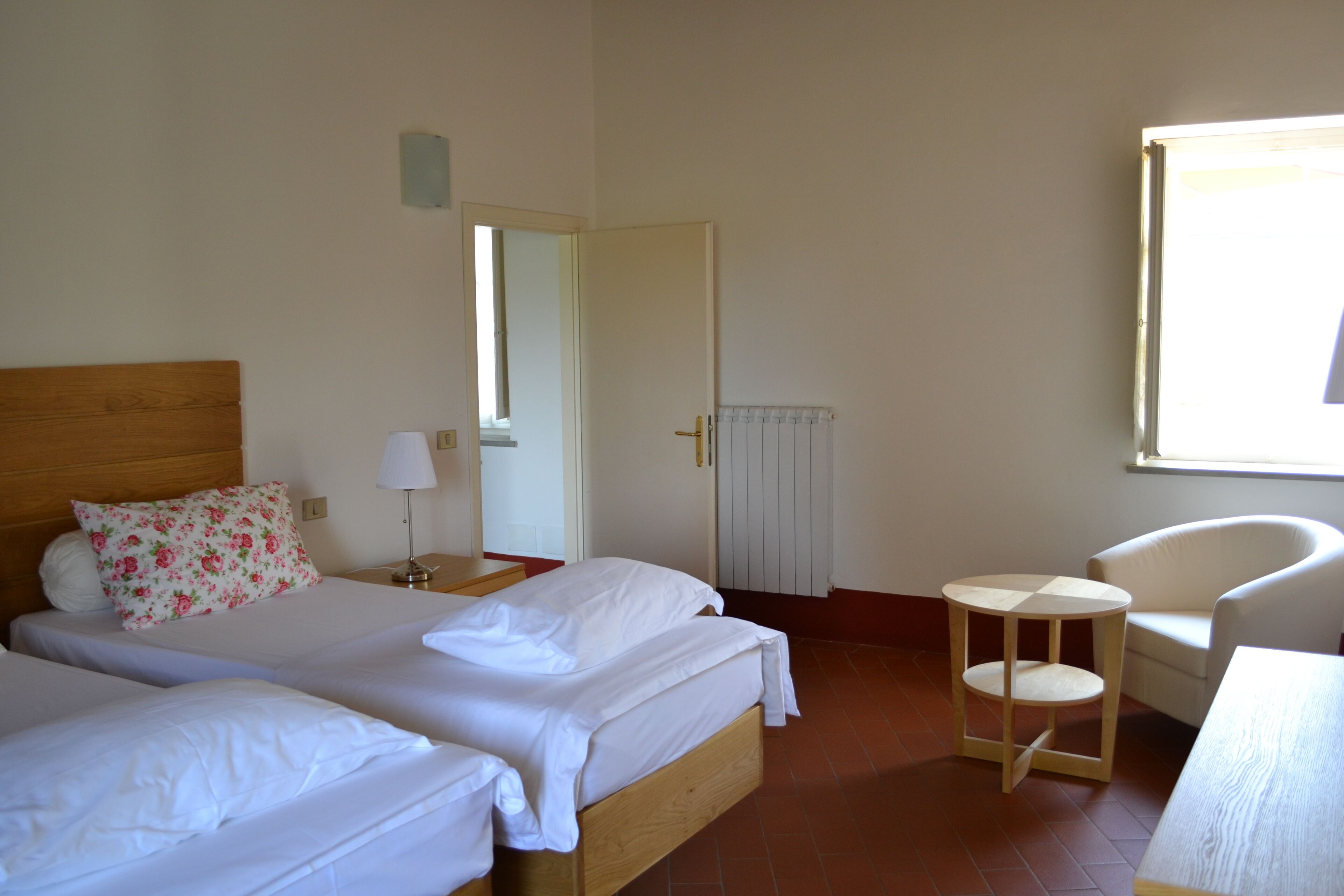 Une chambre d’hôtel avec deux lits, une chaise, une petite table, une table de chevet et une fenêtre.