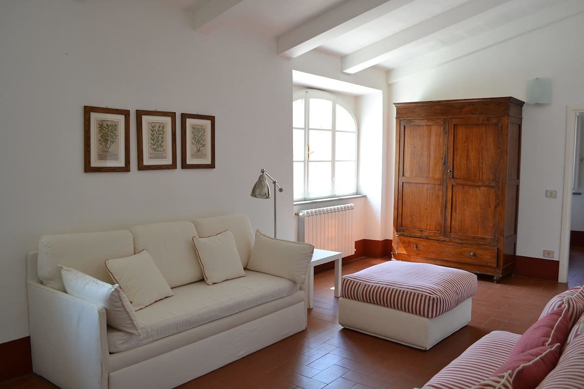 Een woonkamer met een witte bank, een houten kast en een raam met natuurlijk licht.