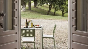 Une porte ouverte donne sur un patio où une table est dressée pour deux personnes, le tout étant entouré de gravier et d’arbres.
