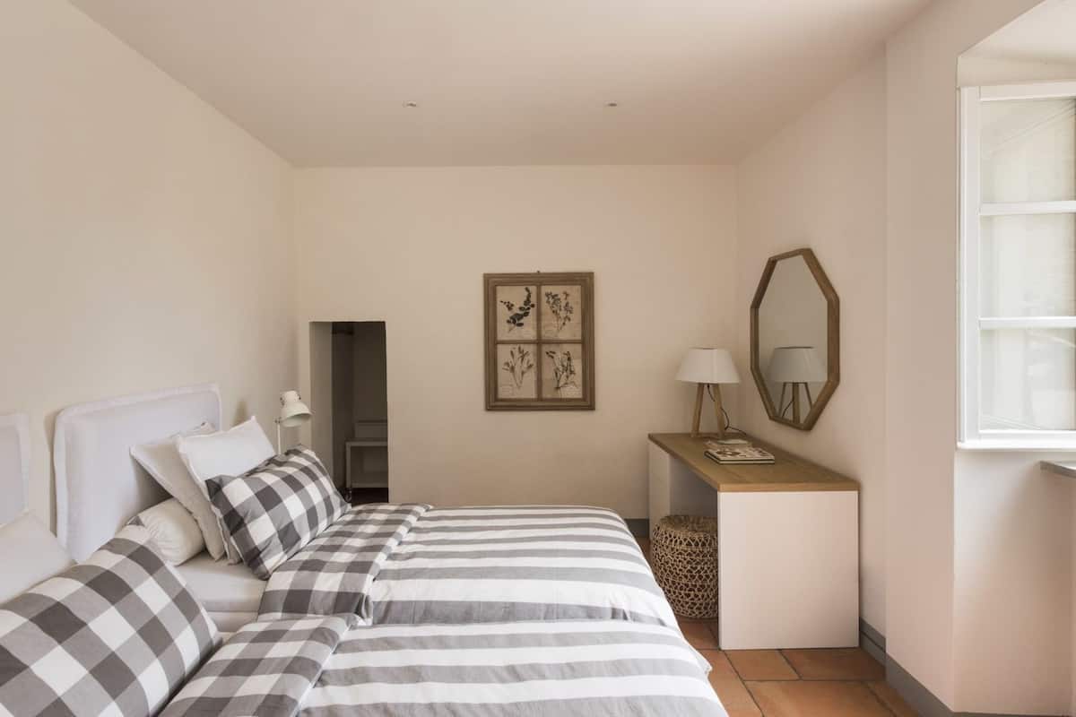 Een slaapkamer met twee bedden, een bureau, een spiegel en kunstwerken in een lijst aan de muur.