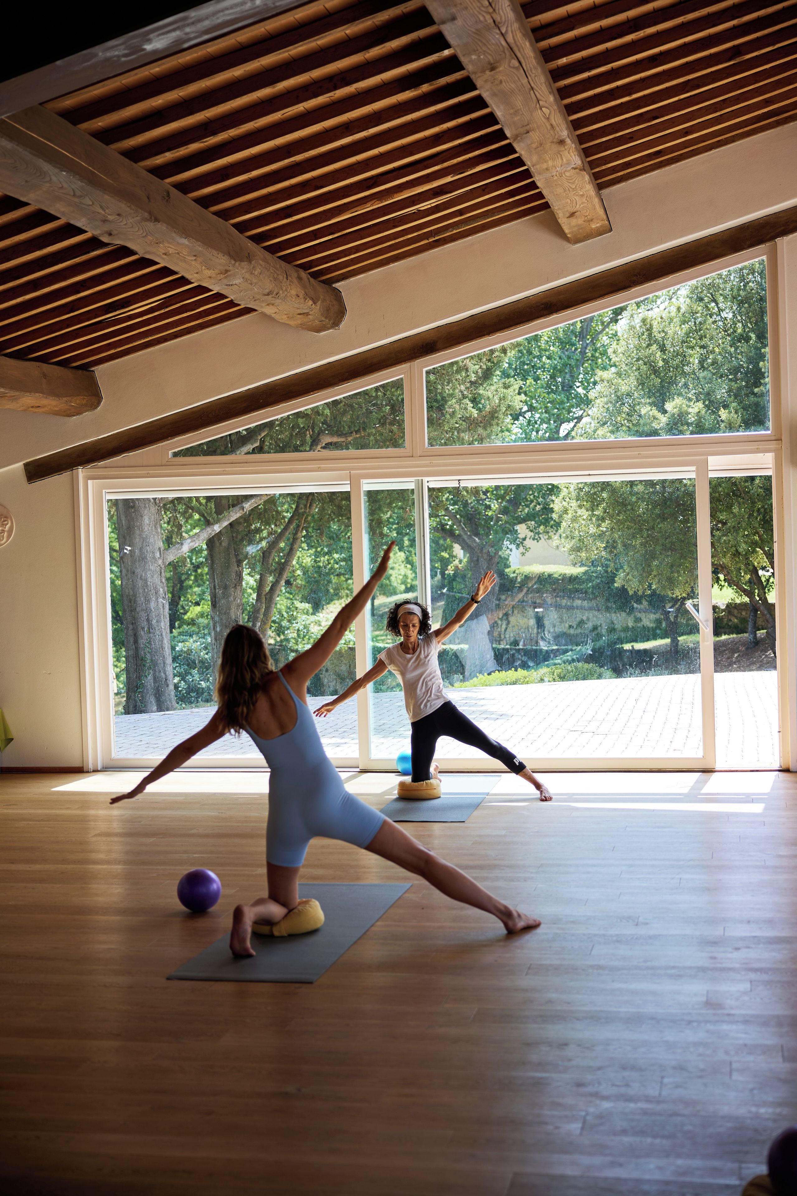Un'ampia stanza con grandi finestre, travi in legno al soffitto e un tappetino da yoga a terra.