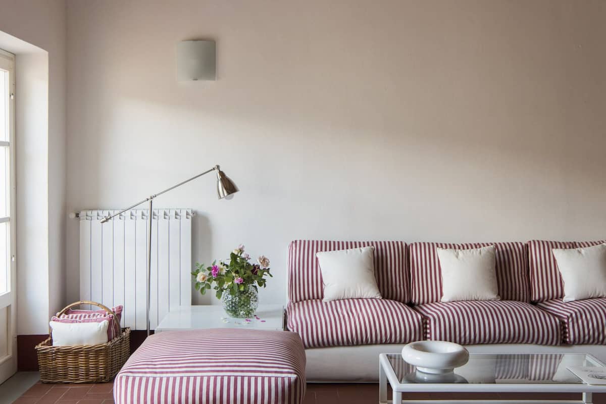 Een woonkamer met een gestreept sofa, een glazen salontafel, een vloerlamp, een vaas met bloemen en een rieten mand.