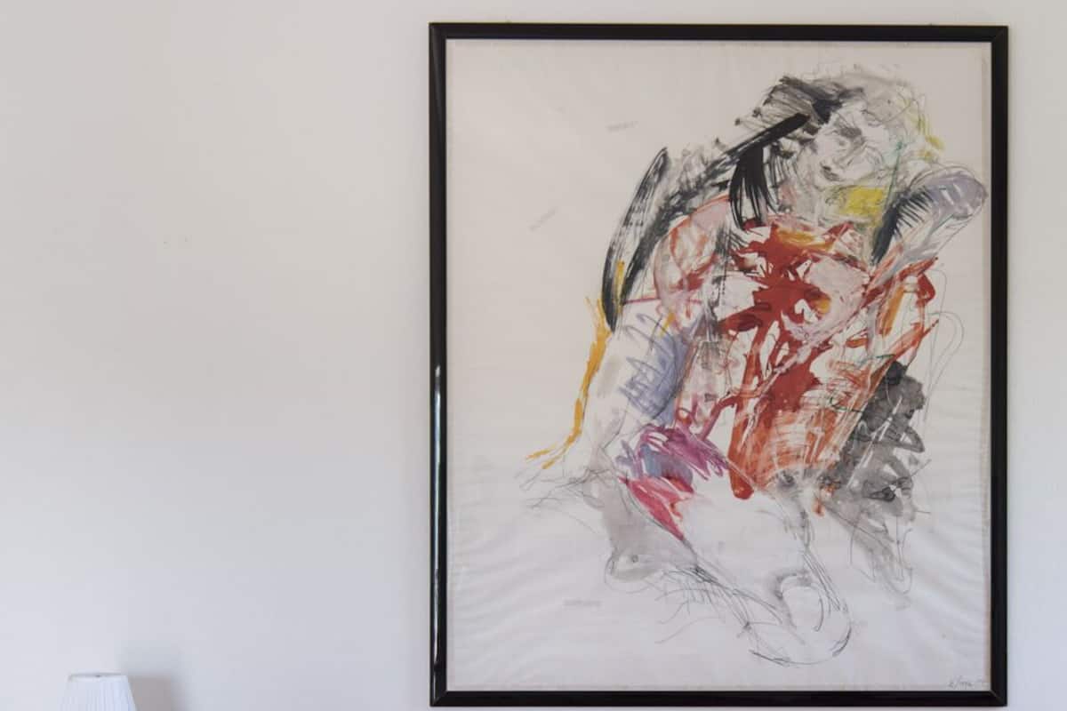 Een woonkamer met een rode bank, een lijst met abstract schilderij en een tafel gedekt met een bloemenprint.