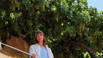 Eine Person steht auf einem Balkon mit Blick auf einen Weinberg und ein Backsteinhaus im Hintergrund.