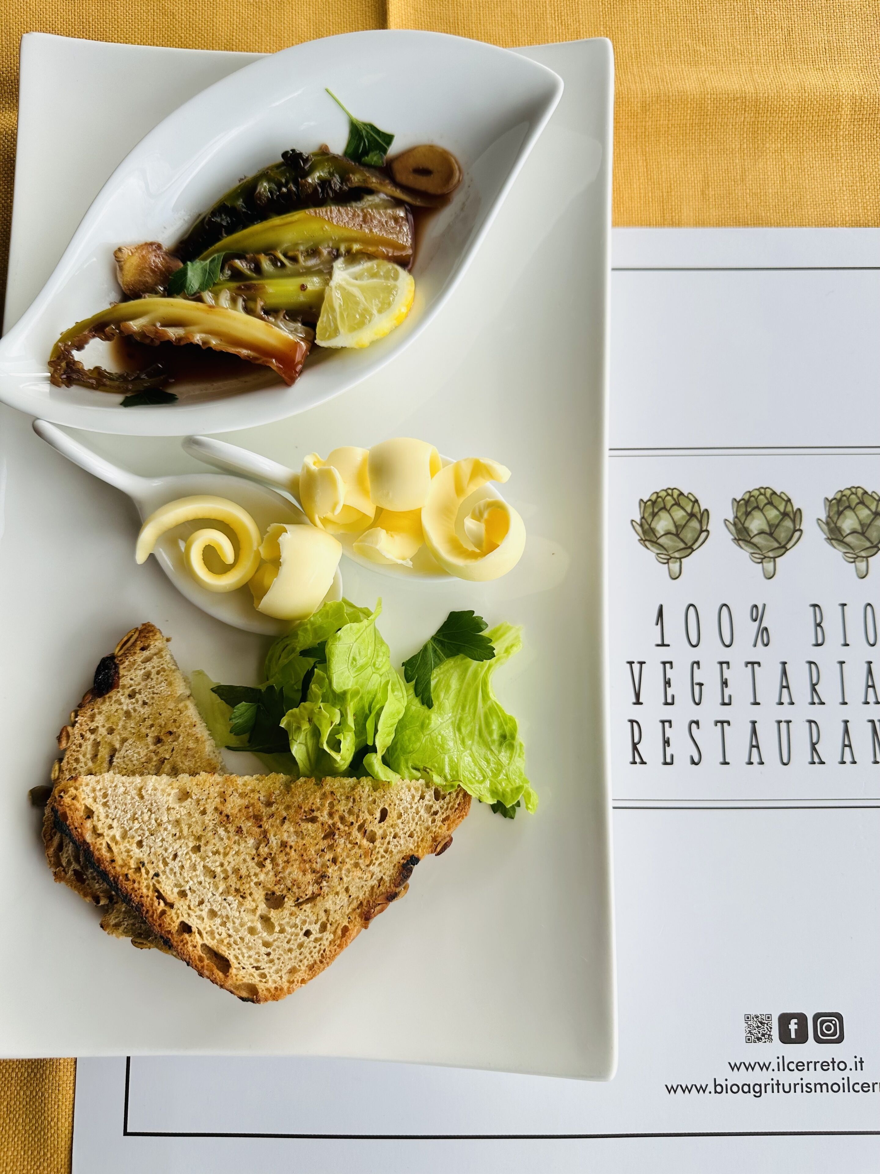 A plate with grilled vegetables, a slice of bread, and a small bowl of sauce.