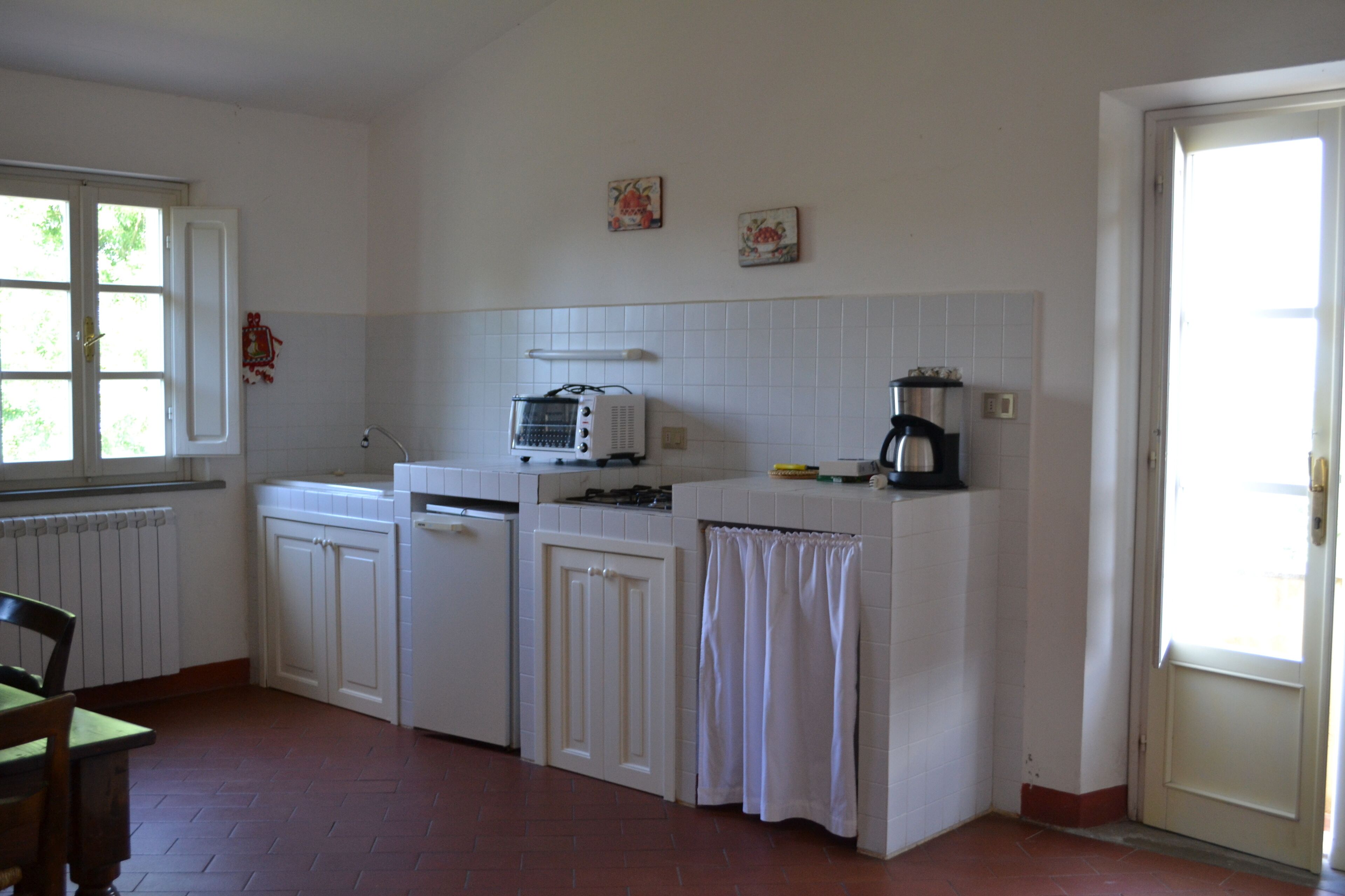 Una cocina con armarios blancos, microondas, cafetera y ventana con vista a la vegetación.