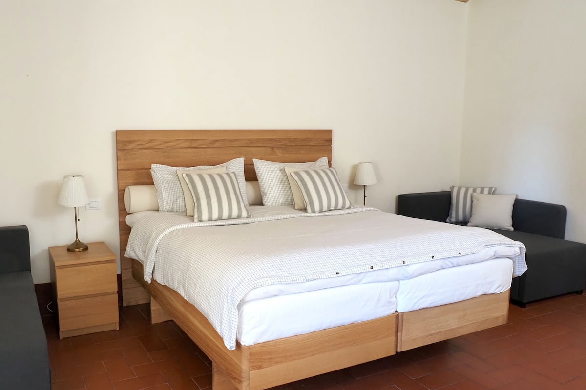 Een slaapkamer met een houten bed, twee nachtkastjes, een bijzettafeltje en twee banken.