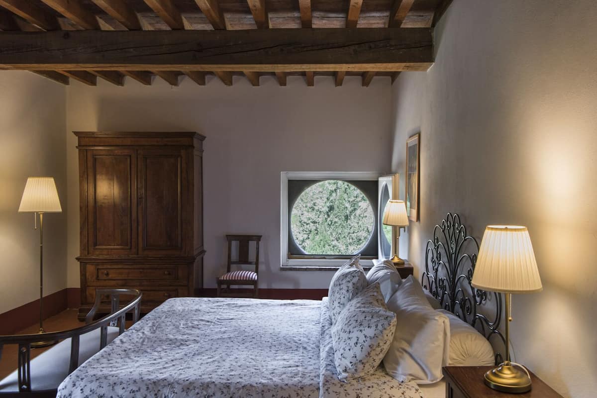 Een slaapkamer met een bed, een houten garderobe, een stoel, een bureau en een raam met uitzicht op groen.