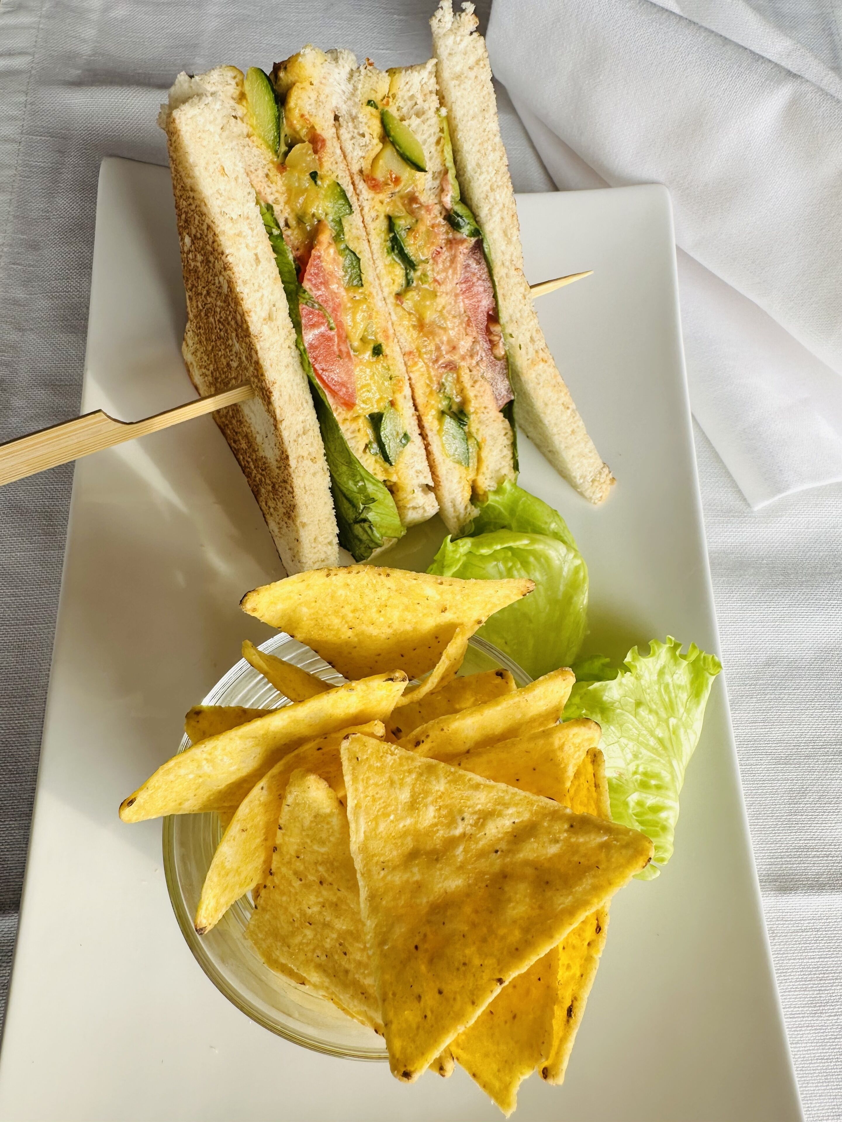 Ein Sandwich mit Salat, Tomate und Käse, sowie eine Portion Tortilla-Chips.