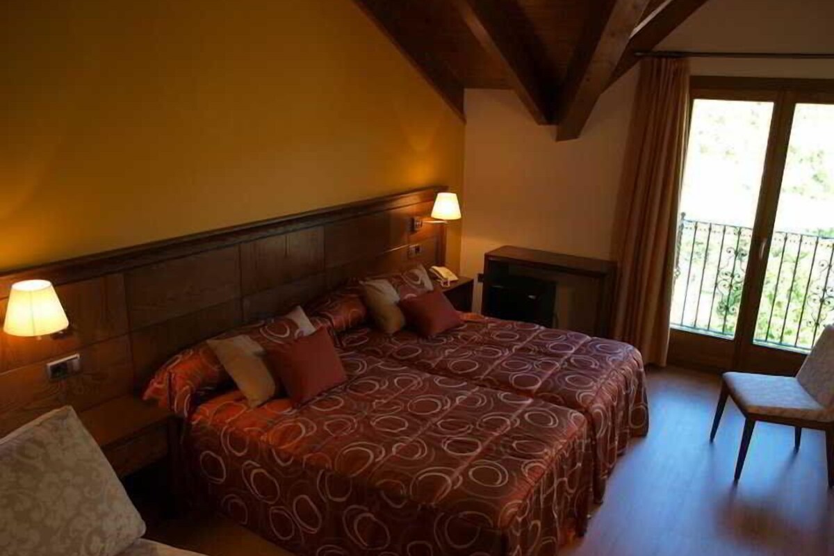 A hotel room with a large bed, two bedside lamps, a small table, and a chair.