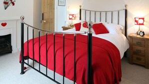 A bedroom with a metal bed frame, red bedding, bedside tables with lamps, a wooden door, and a fireplace.