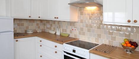 Una cocina moderna con armarios blancos, horno empotrado, estufa y salpicadero con baldosas color beige.