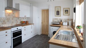 A modern kitchen with white cabinetry, a built-in oven, a dishwasher, and a stainless steel sink. There are two framed pictures on the wall and a wooden door in the background.