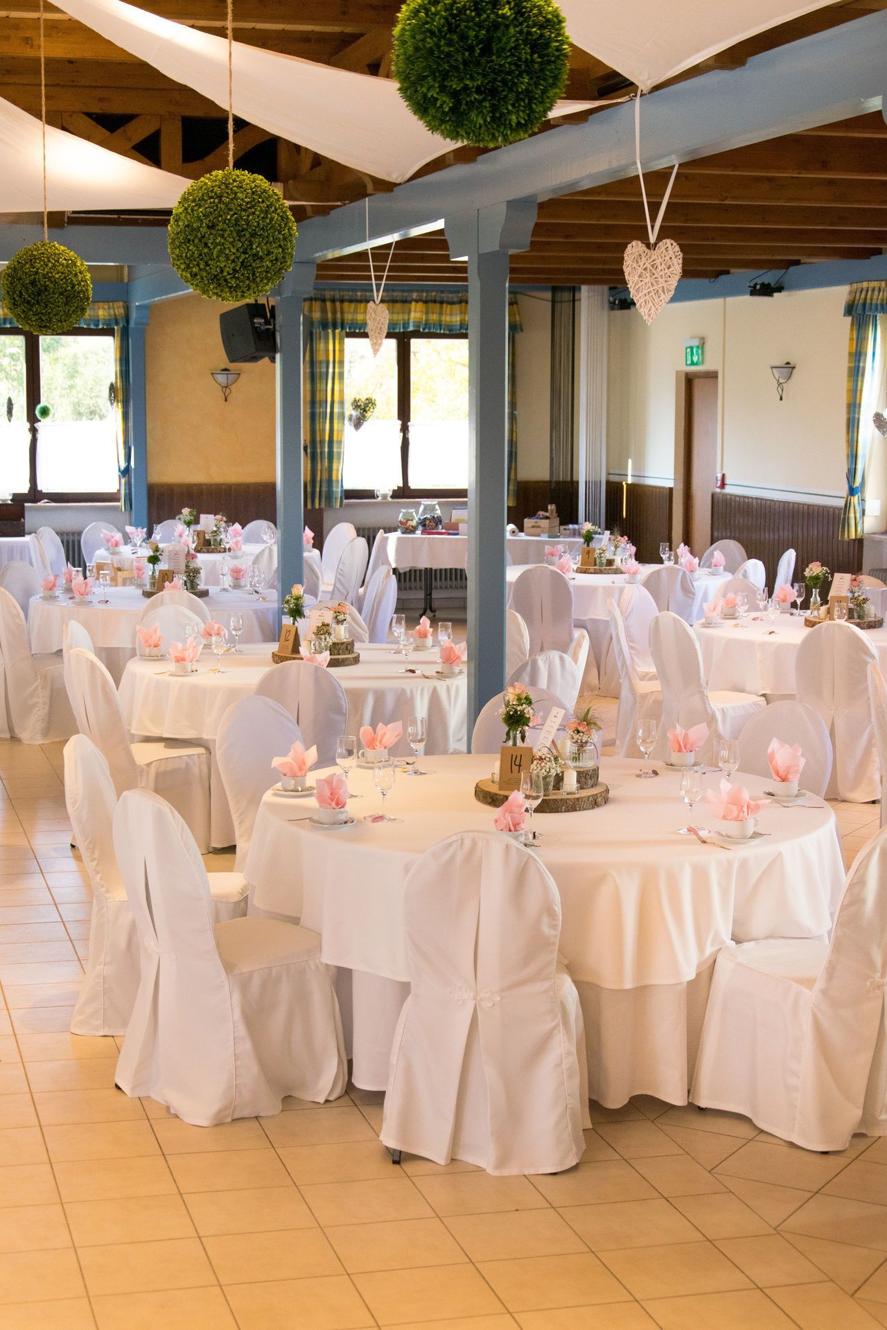 A banquet hall with round tables covered in white tablecloths, white chairs, and floral centerpieces.