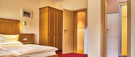 Una habitación de hotel con una cama, un armario de madera, una mesita de noche y una alfombra roja.