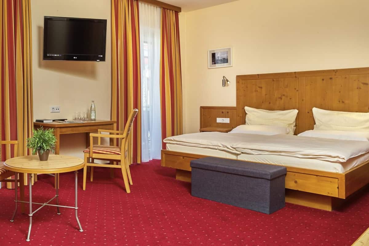 Une chambre d’hôtel avec un lit, un bureau, une chaise, une télévision et une petite table sur laquelle est posée une plante.