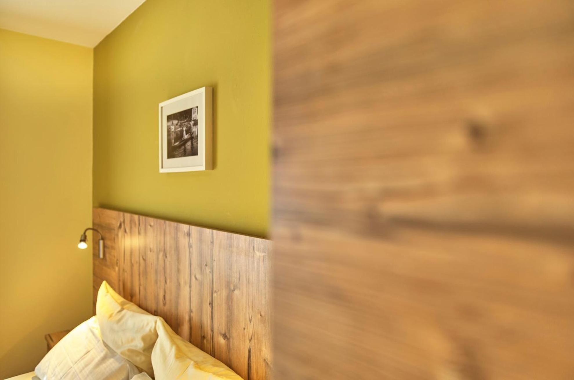 Una habitación con cabecera de madera, un cuadro en la pared y una lámpara de noche.