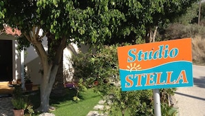 A sign for "Studio Stella" in a garden setting with potted plants and a stone pathway. - Studios Stella (Agios Vasileios)