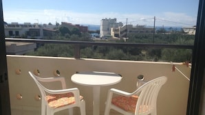 A balcony with two white plastic chairs and a small round table, overlooking a cityscape with buildings and a distant view of the sea. - Studios Stella (Agios Vasileios)