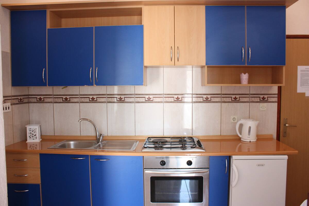 A kitchen with blue cabinets, a stainless steel sink, a gas stove, an oven, and a white refrigerator.