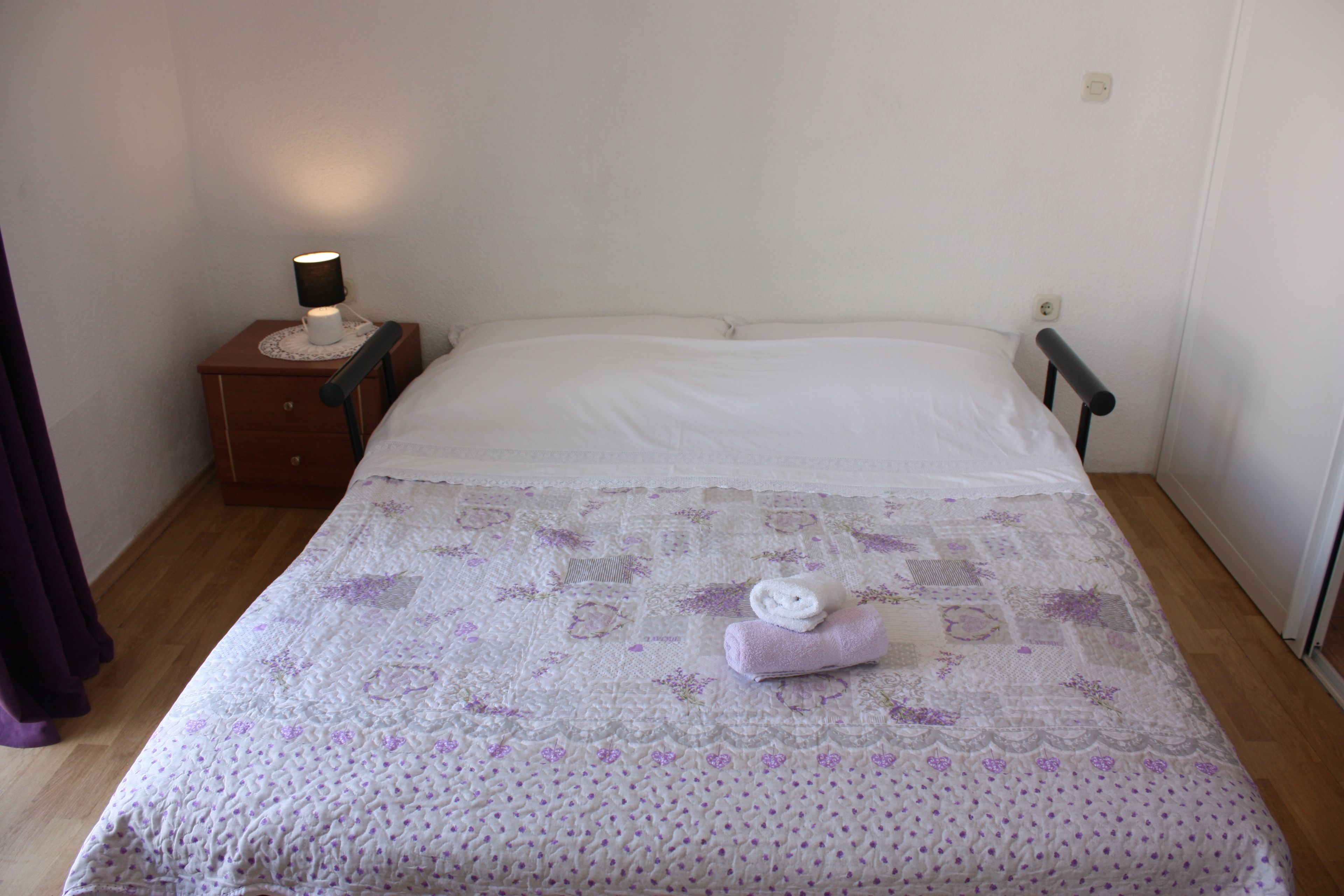 A neatly made bed with a patterned bedspread and two rolled towels on it.